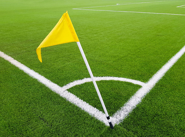 サッカー場の角に黄色の旗。サッカーボールのコーナーキックのための場所。サッカー選手のためのホワイトラインマーキングスポーツフィールド. - 写真・画像