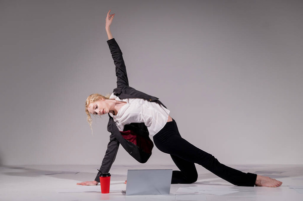Uma bailarina vestida em um terno de negócios posa para um laptop e bebe café. Mulher flexível trabalha no computador - Foto, Imagem