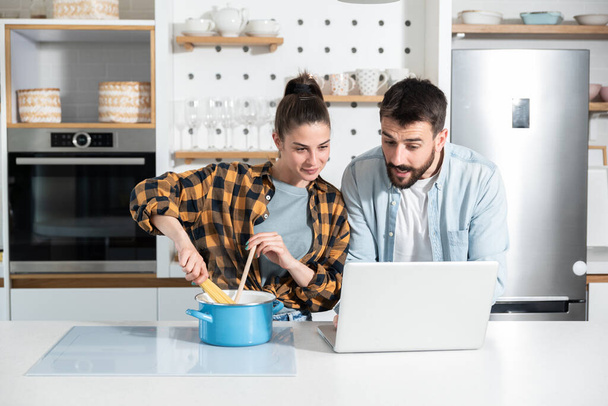 Happy young couple is having fun while cooking pasta in the kitchen for dinner and reading recipes from the internet, happy couples food concept - Photo, image