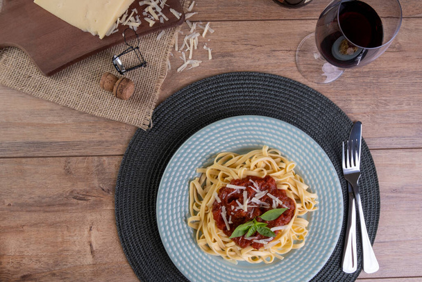 dish with noodles topped with tomato sauce, with a glass of sparkling red wine. - Foto, Imagem