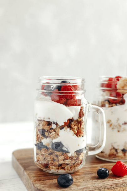 A healthy, dietary breakfast or snack of granola or oatmeal muesli with yoghurt and fresh wild berries. Light background and vertical photo. Copy space - Photo, image
