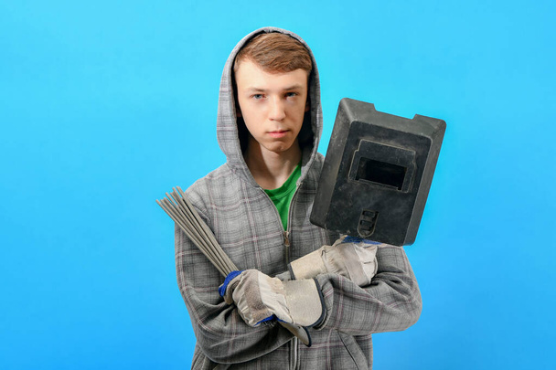 Young welder with electrodes and welding shield on a blue background. - Foto, afbeelding