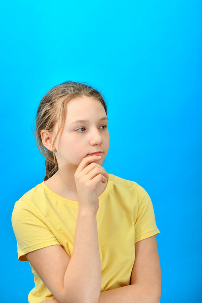 Portrait of a pensive young girl in yellow clothes on a blue background. - Foto, imagen