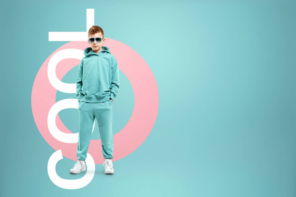 Portrait, cute stylish boy in a blue suit on a blue background. Studio portrait of a child, modern design, trendy background, turquoise. The lettering is cool - Фото, изображение
