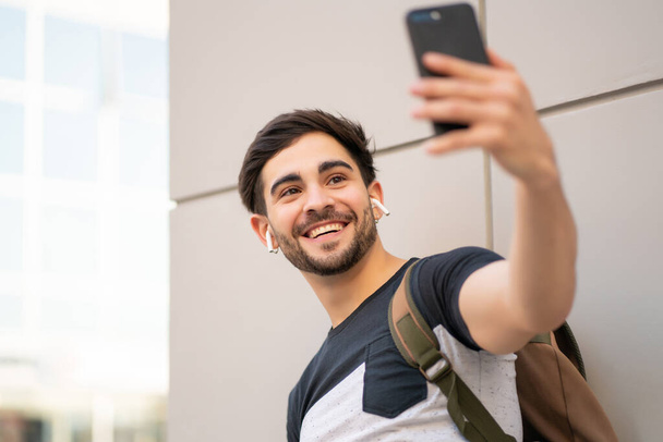 Portrait of young man taking a selfie with phone outdoors. - Foto, Imagem