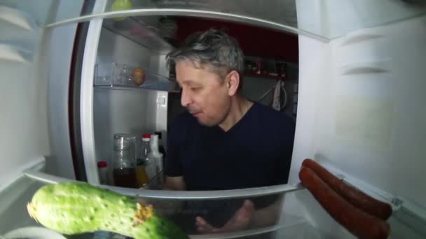 Een ongeschoren man met een kater doorzoekt de koelkast voor een drankje en iets te eten. - Video