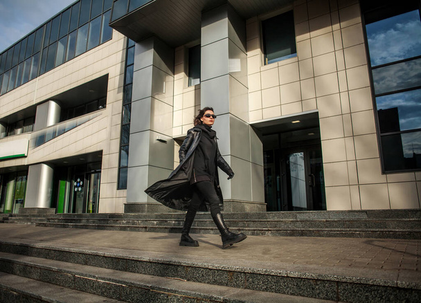 Frau in schwarzem Ledermantel und Brille läuft eilig aus dem Gebäude des Geschäftszentrums - Foto, Bild