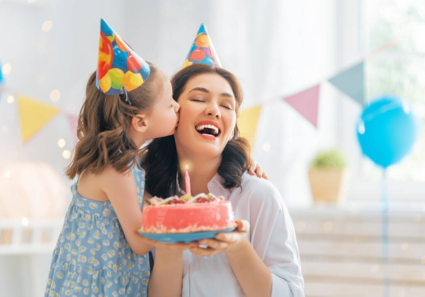The kid is blowing out the candles on the cake. Mother and daughter are celebrating birthday. - Foto, Imagen