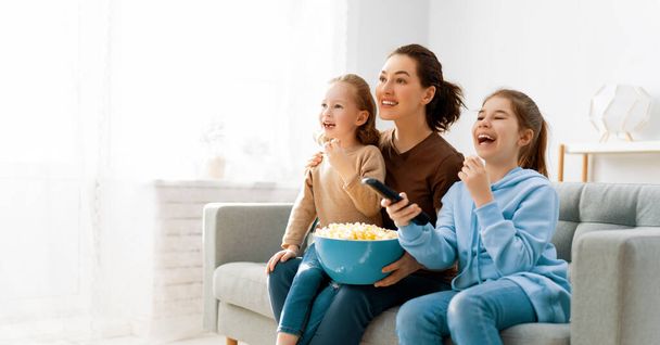 Feliz familia viendo televisión, películas con palomitas de maíz por la noche en casa. Madre e hijas pasando tiempo juntas. - Foto, Imagen