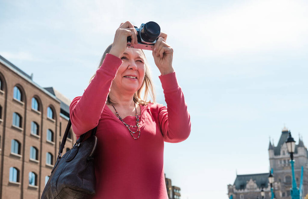 Dojrzała blondynka robi zdjęcie przy Tower Bridge. Używa kamery filmowej, a most jest na tle.. - Zdjęcie, obraz