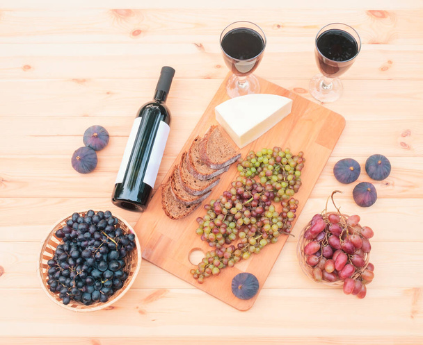 Two glasses of red wine, bottle of red wine, figs, cheese, bunches of grape and bread on wooden table. Top view. - Foto, immagini