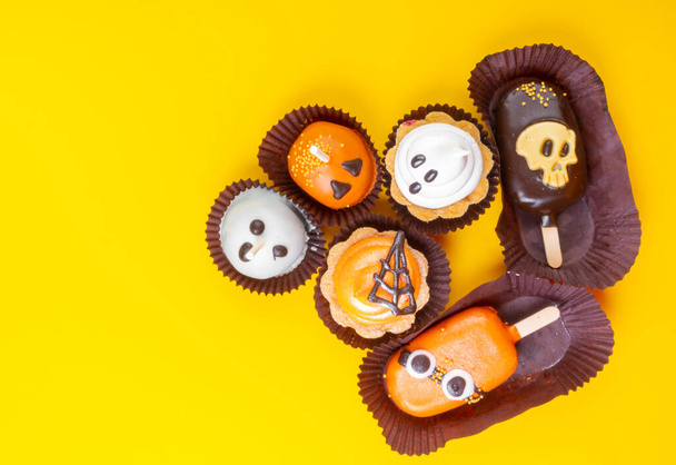 Süßigkeiten und Leckereien zu Halloween auf gelbem Hintergrund. Geist, Totenkopf und Monster, gespenstisches Symbol auf Party-Desserts. Kopierraum - Foto, Bild