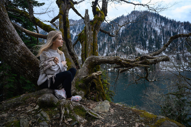 Mädchen sitzt auf einem Baum und meditiert auf blauem See-Hintergrund. Ritsa-See in Abchasien - Foto, Bild