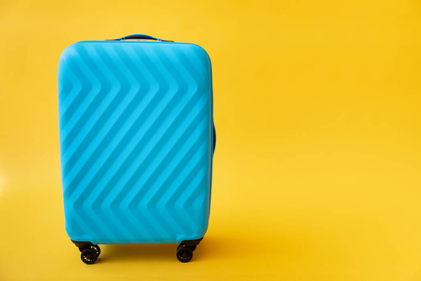 Blue suitcase against yellow background. Summer vacation and travel concept - Fotó, kép