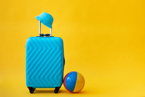 Blue suitcase against yellow background. Summer vacation and travel concept - Fotó, kép