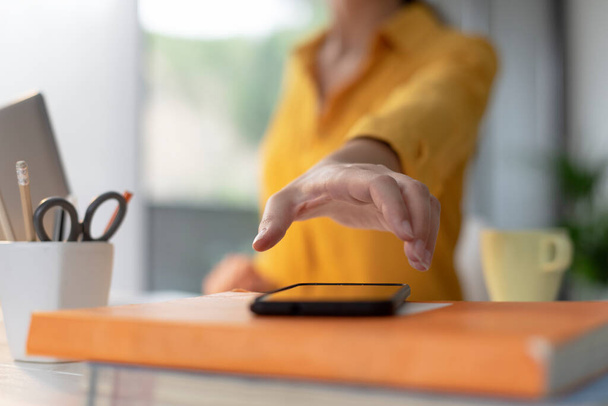Woman sitting at desk and working, she is taking her smartphone and answering a phone call, hand close up - Photo, Image