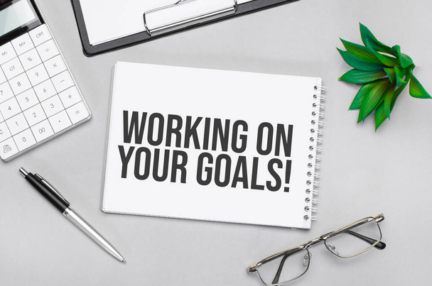 Writing text showing working on your goals. Calculator,pen,plan,glasses and black folder on grey background - Foto, Bild