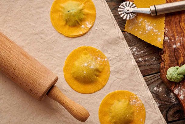 Tasty raw homemade ravioli pasta with spinach and ricotta on wooden rustic background. Process of making Italian ravioli.  - 写真・画像