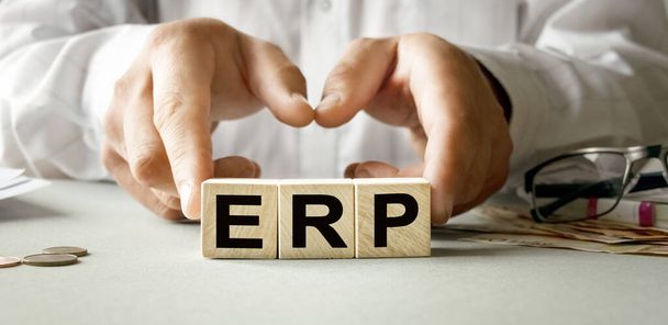 ERP inscription on the texture of wooden cubes. A business man holds a cube in his hand. An inscription on a financial, business or economic theme. - 写真・画像