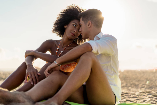 A fajok közötti szerelmespár gyengéden megérinti a homloka ül a strandon a nyáron. Multiracionális romantikus fiatalok koncepciója. - Fotó, kép