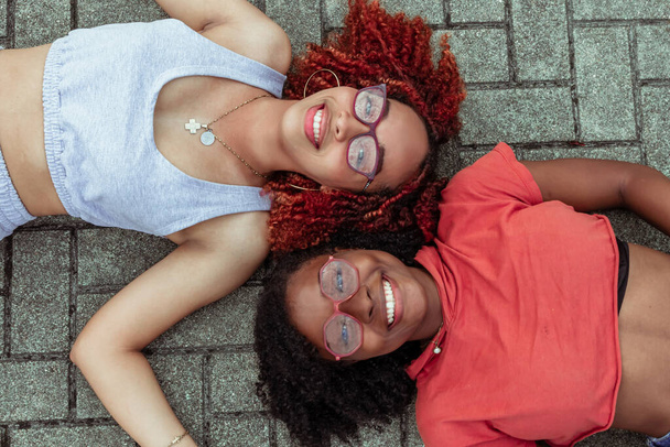 Jovenes mujeres afro con lentes tendidas en el suelo sonriendo - Foto, afbeelding
