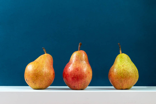 three pears on white podium against blue background, minimal still life - 写真・画像