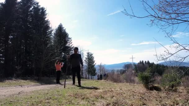 Limanowa, Poland: Ένας άνθρωπος με σακίδιο, μπουκάλι νερό και ένα ξύλινο ραβδί, ενώ πεζοπορία ή πεζοπορία στα πολωνικά βουνά προς ένα ορόσημο του μεταλλικού σταυρού κατά τη διάρκεια της ημέρας - Πλάνα, βίντεο