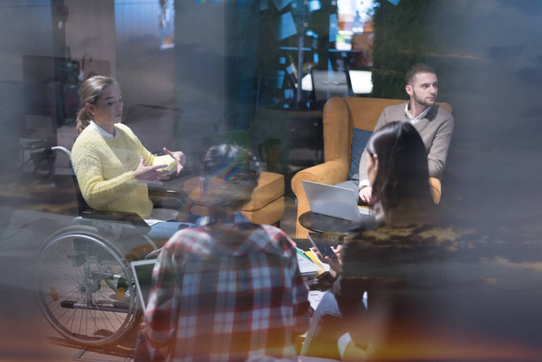 Trabalhadores de escritório e pessoa em uma cadeira de rodas discutindo momentos de negócios em um escritório moderno. Incapacidade e conceito de negócio - Foto, Imagem