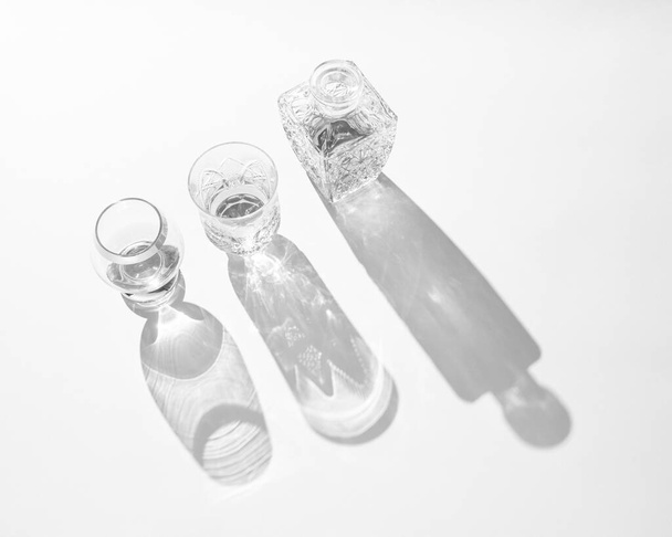 Crystal bottle and two glasses with long shadows. Black and white composition - Фото, зображення
