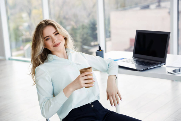 Joven mujer de negocios hermosa bebe café durante un descanso en la oficina. Concepto de relajación  - Foto, Imagen