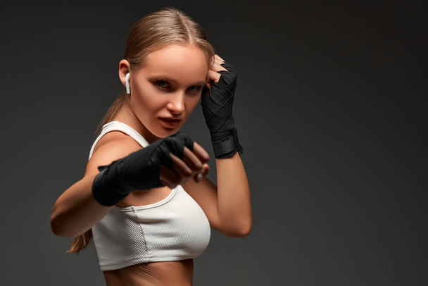 Sporting woman in boxing bandages in studio looking at camera. Isolated gray background. Copy space. - 写真・画像