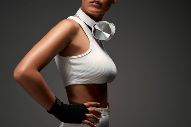 Beautiful young woman wearing gym clothes and using headphones of neck. Isolated grey background. Cropped photo. - Φωτογραφία, εικόνα