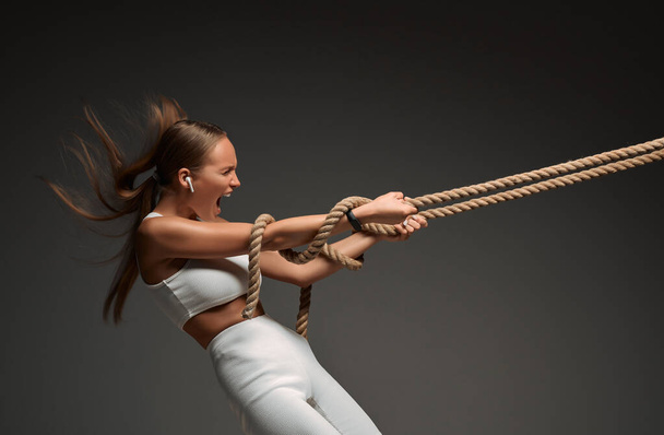 Strong woman pulling rope on grey background. Strength and motivation concept. Side view. - 写真・画像