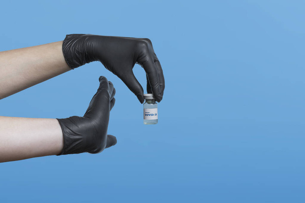 Σταματήστε το covid.Vaccination έννοια. Ανάπτυξη και δημιουργία εμβολίου κατά του coronavirus. Ιατρική έννοια πάνω από το μπλε φόντο. Χέρια γιατρού σε μαύρα ιατρικά γάντια με εμβόλιο COVID-19. - Φωτογραφία, εικόνα