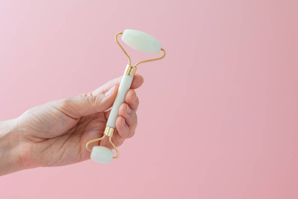 White quartz massager on a womans hand on a pink background, massager to tighten the skin on the face and neck to eliminate wrinkles and aging effects - Φωτογραφία, εικόνα