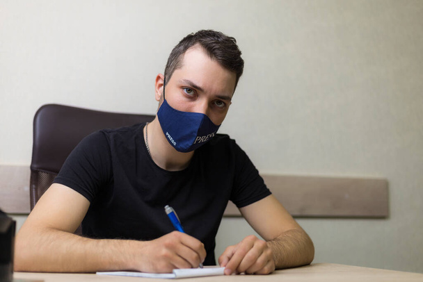 Jeune homme beau dans un masque avec l'inscription presse travaille dans le bureau - Photo, image