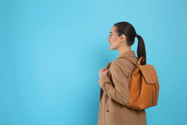 Beautiful young woman with stylish leather backpack on turquoise background. Space for text - Фото, изображение