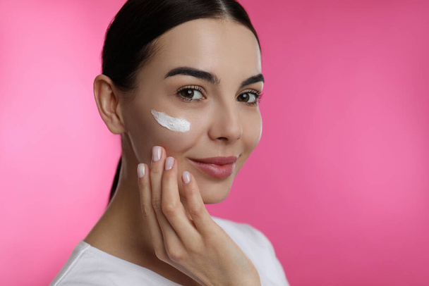 Young woman applying facial cream on pink background - Foto, Imagem