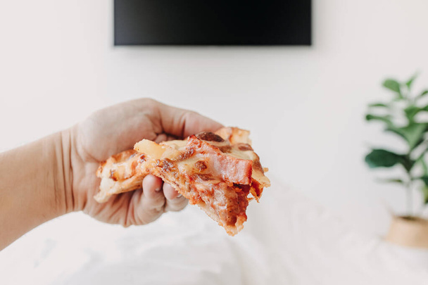 Wer mit Pizza im Bett liegt, sieht einen Fernseher. Konzept des Daheimbleibens. - Foto, Bild