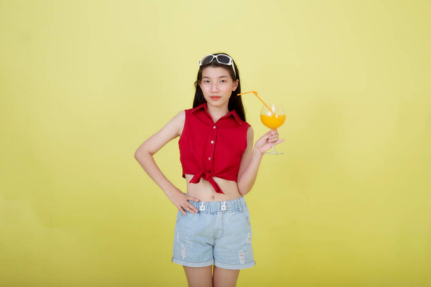 Portrait d'une belle jeune femme asiatique buvant du jus d'orange sur fond jaune - Photo, image