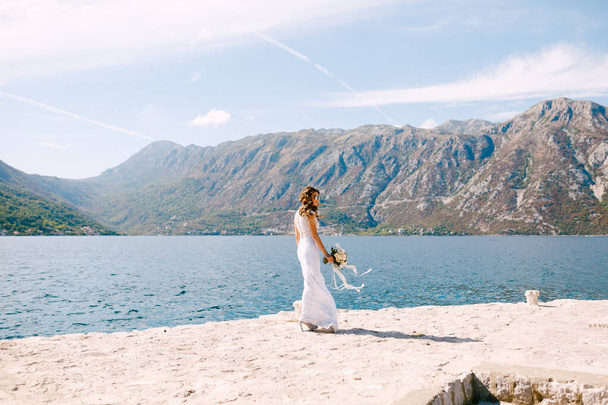 Linda noiva caminha ao longo da costa ensolarada com um lindo buquê de casamento de flores - Foto, Imagem