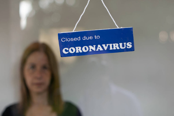 Vrouw achter de deur van haar bedrijf gesloten door covid aangegeven door een teken - Foto, afbeelding