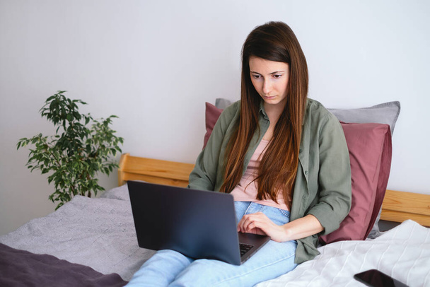 Young woman sitting in bed and working with laptop. Free time at home. - Photo, image