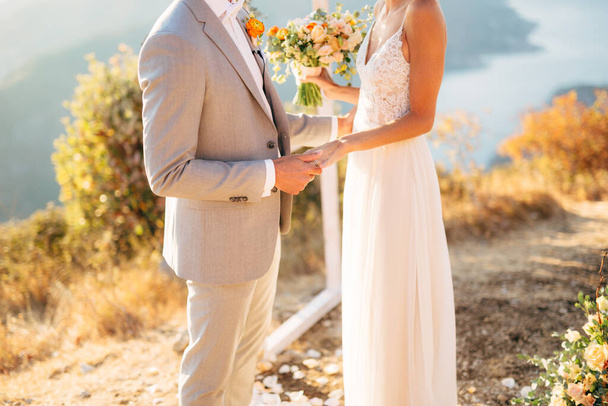 Жених и невеста стоят на горе Ловсен возле свадебной арки и держатся за руки. - Фото, изображение