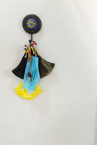 Μάσκες προσώπου διαφόρων τύπων που κρέμονται με ένα μάτσο κλειδιά στον τοίχο - Φωτογραφία, εικόνα