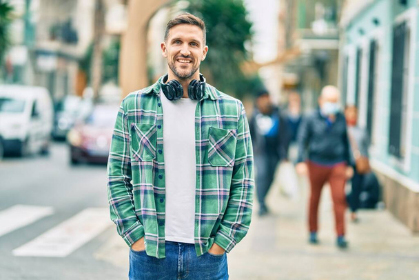 Молодий білий чоловік посміхається щасливий, використовуючи навушники в місті
. - Фото, зображення