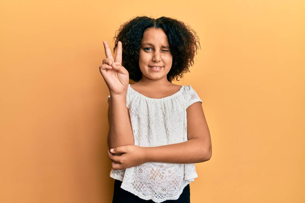 Young little girl with afro hair wearing casual clothes smiling with happy face winking at the camera doing victory sign. number two.  - Photo, Image