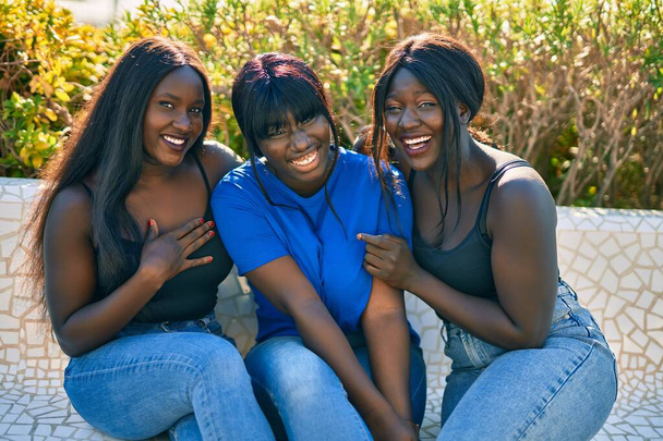 Három afro-amerikai barát boldogan mosolyog a padon ülve a parkban.. - Fotó, kép