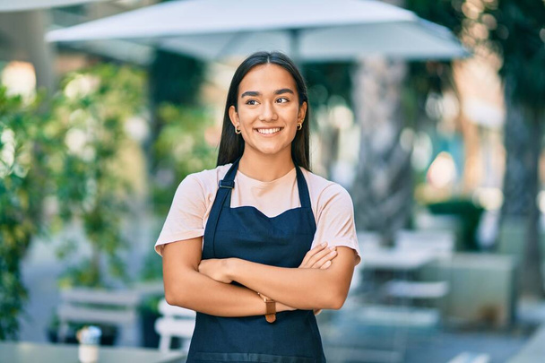 Young latin barista girl with arms crossed smiling happy at the coffee shop - Foto, Imagem