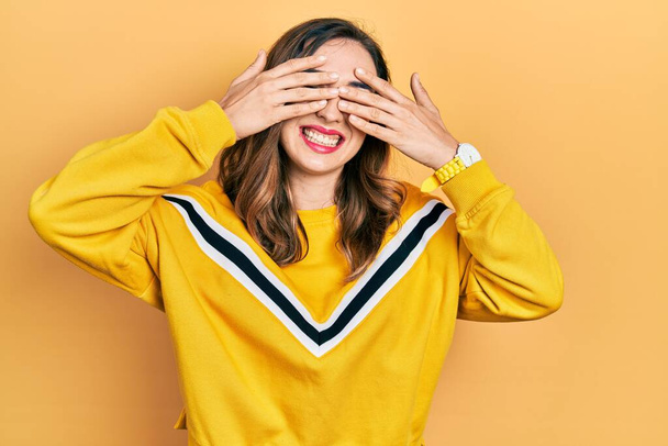Young hispanic girl wearing casual clothes covering eyes with hands smiling cheerful and funny. blind concept.  - Фото, изображение